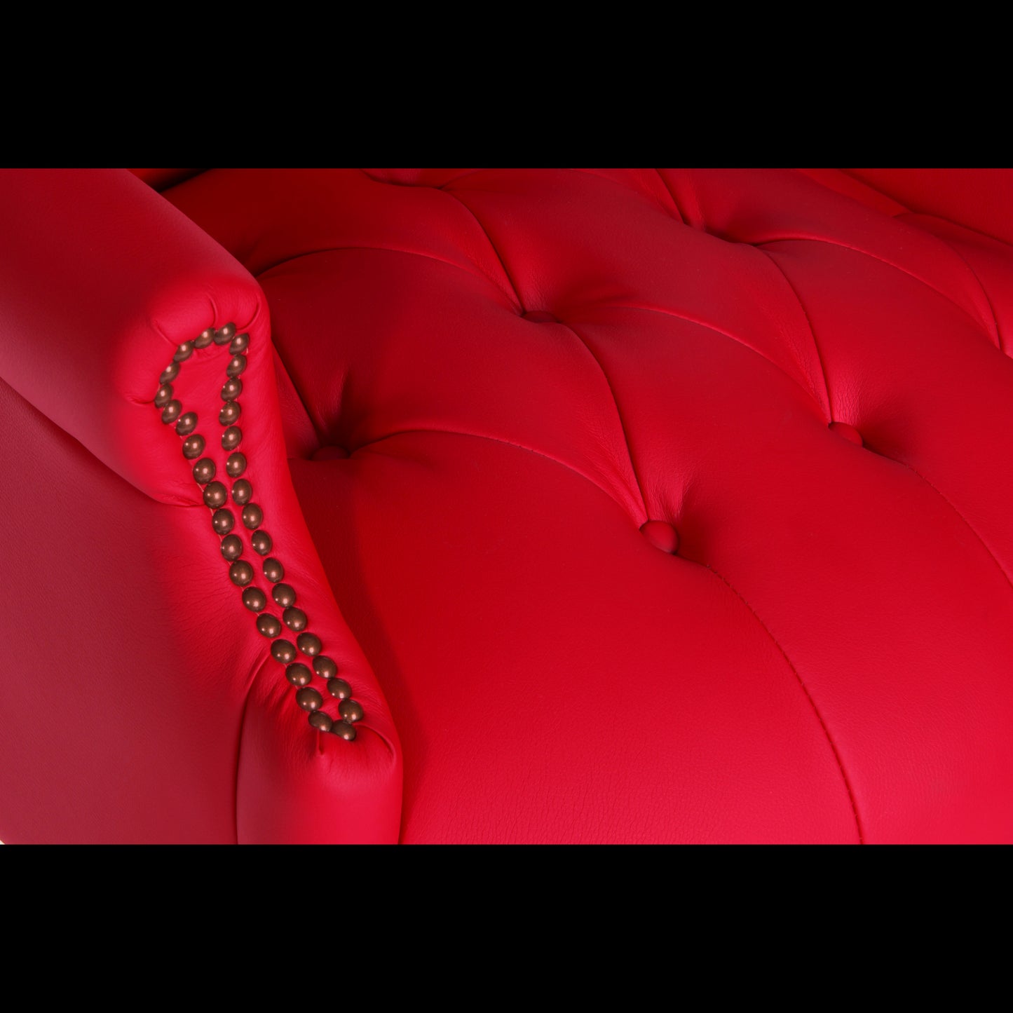 Close-up of a red tufted armchair with decorative nailhead trim.