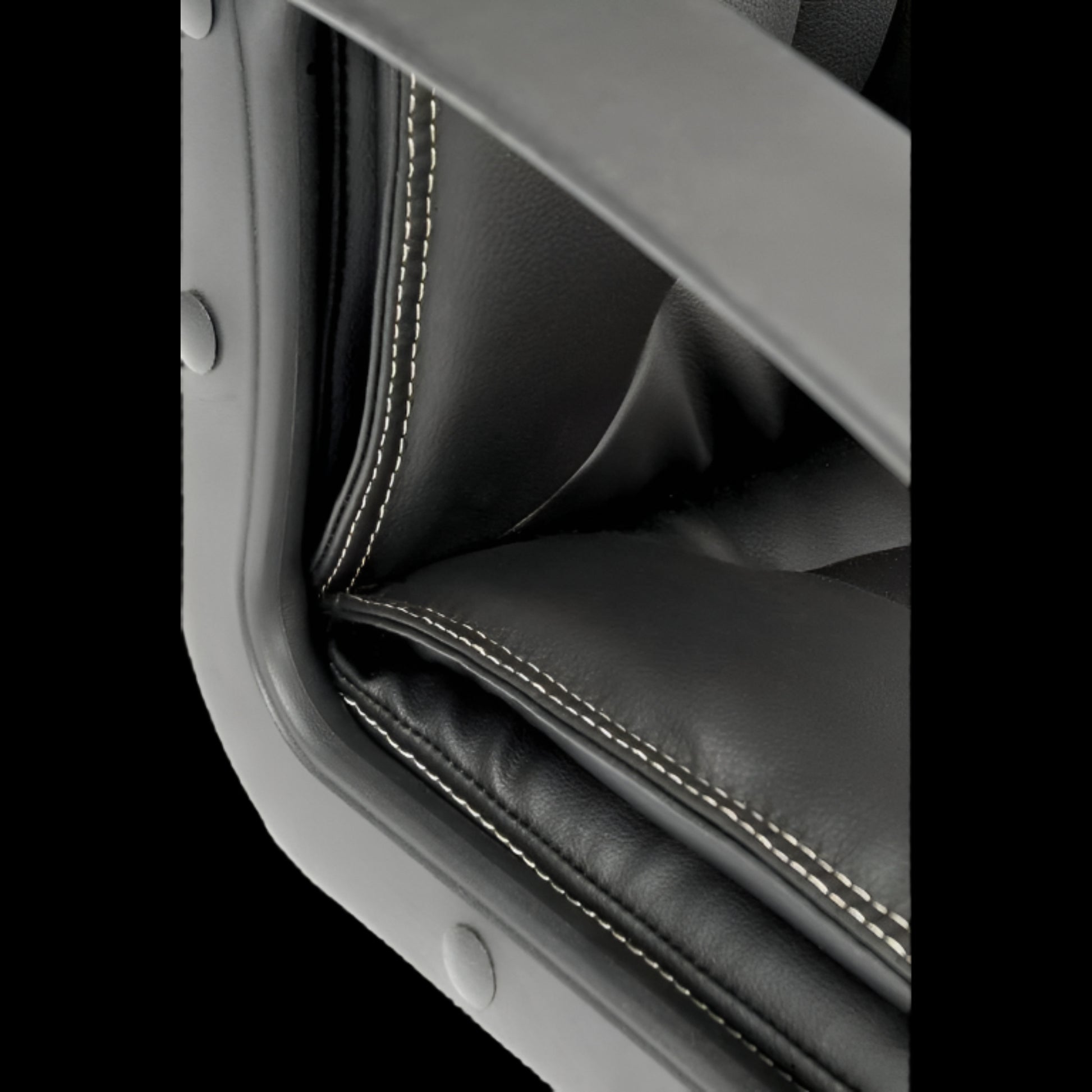 Close-up of a black leather seat with stitching detail on a black background