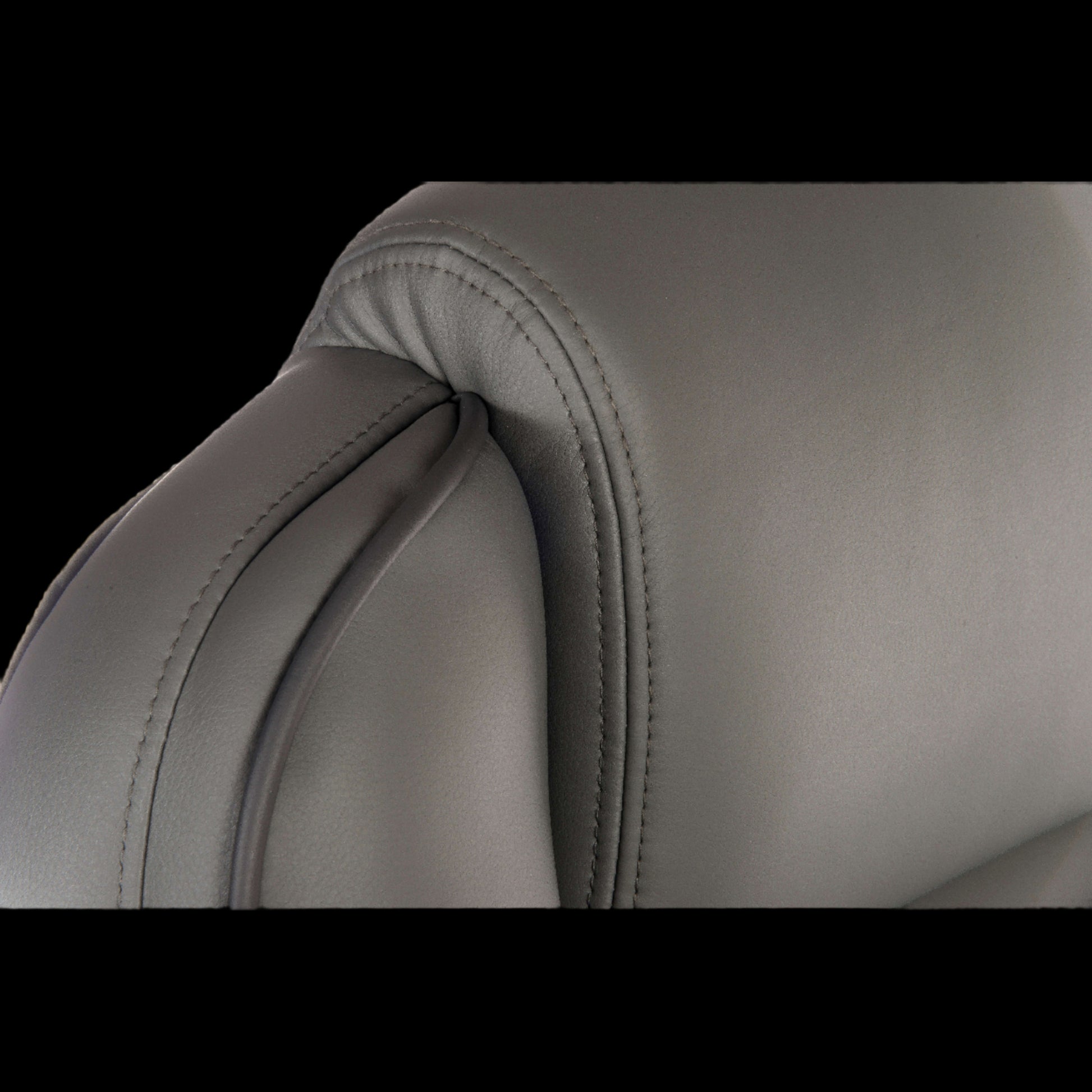 Close-up of a gray leather chair with visible stitching on a black background