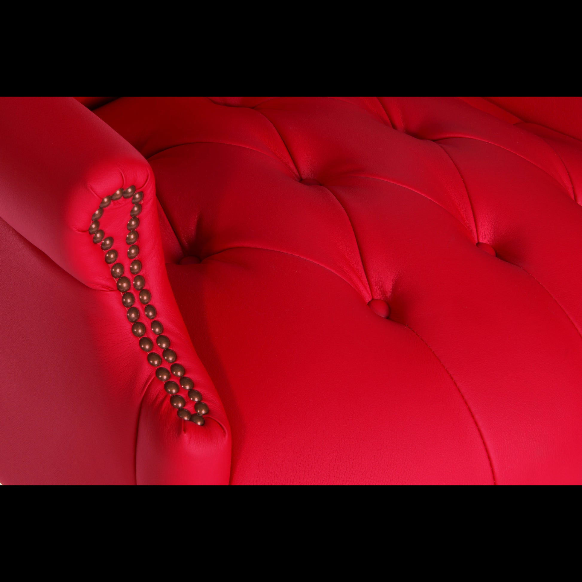 Close-up of a red tufted armchair with decorative nailhead trim.