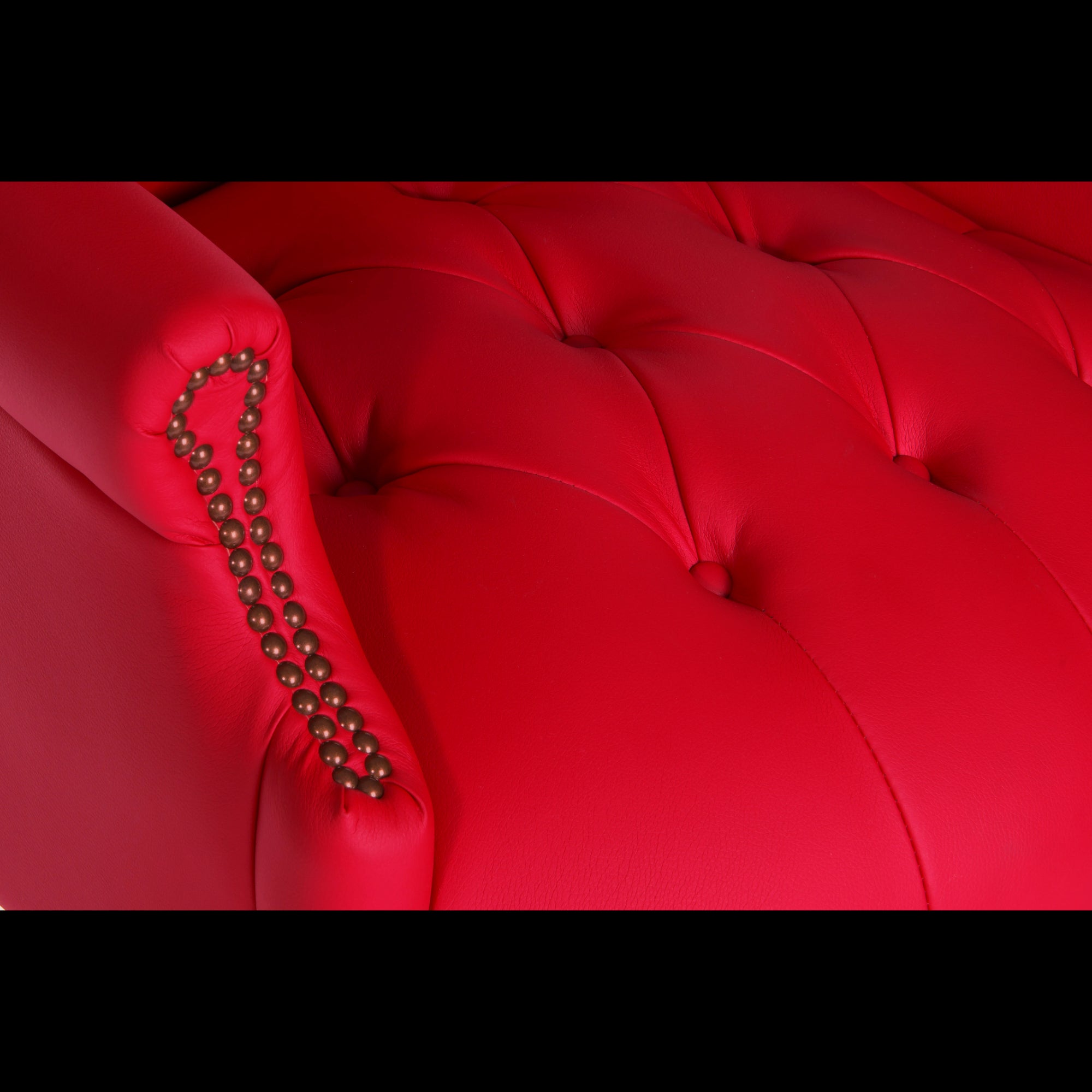 Close-up of a red tufted armchair with decorative nailhead trim.