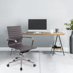 Modern office desk with a chair and computer setup against a light gray wall.