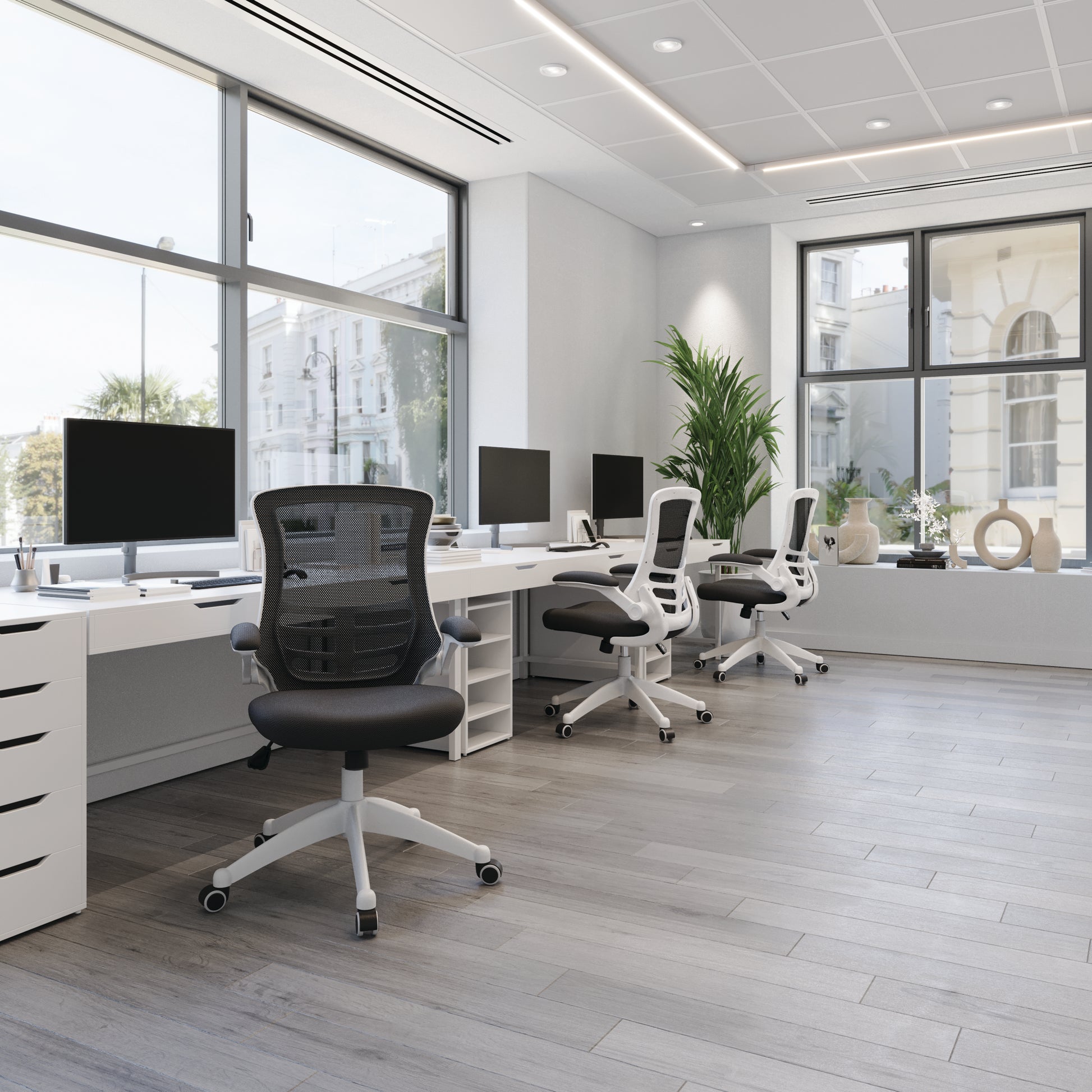 Modern office setup with desks, chairs, and computer monitors in a bright room.