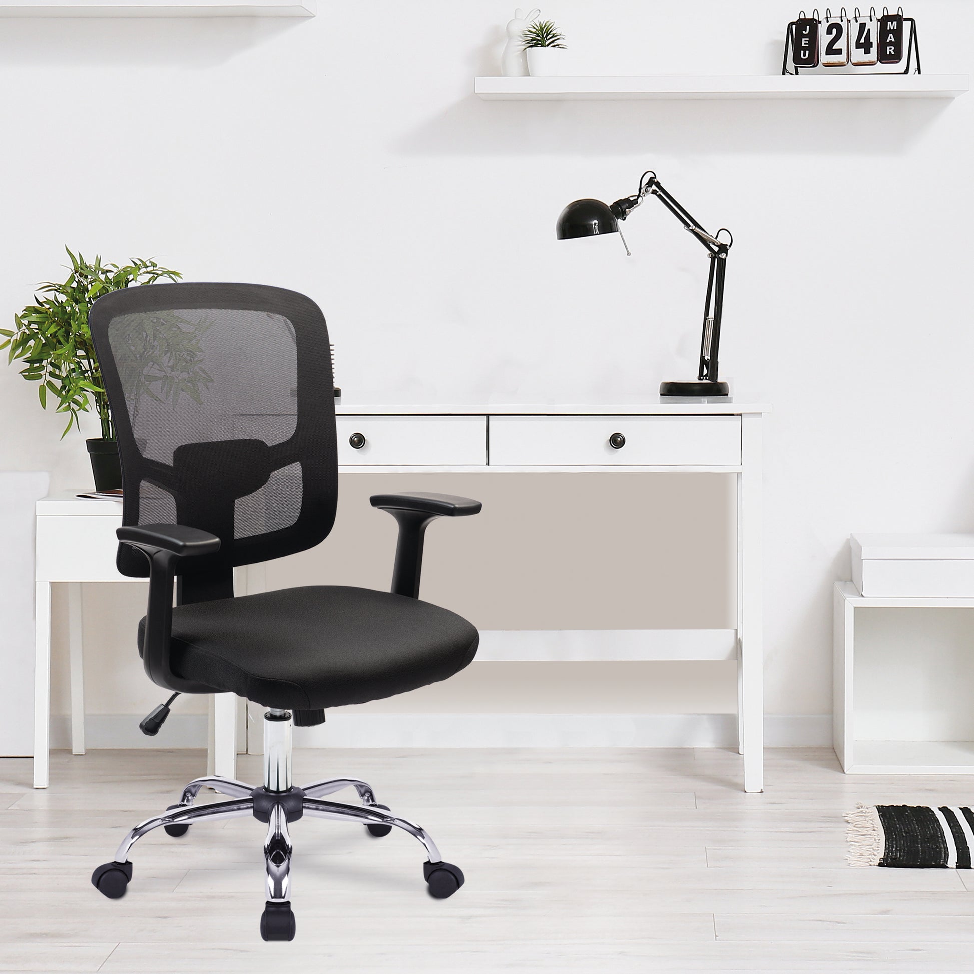 Black office chair in front of a white desk with a lamp and plant.