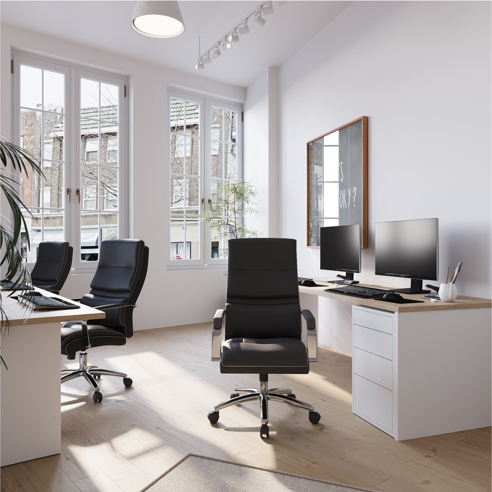 Modern office setup with desks, chairs, and computer monitors in a bright room.